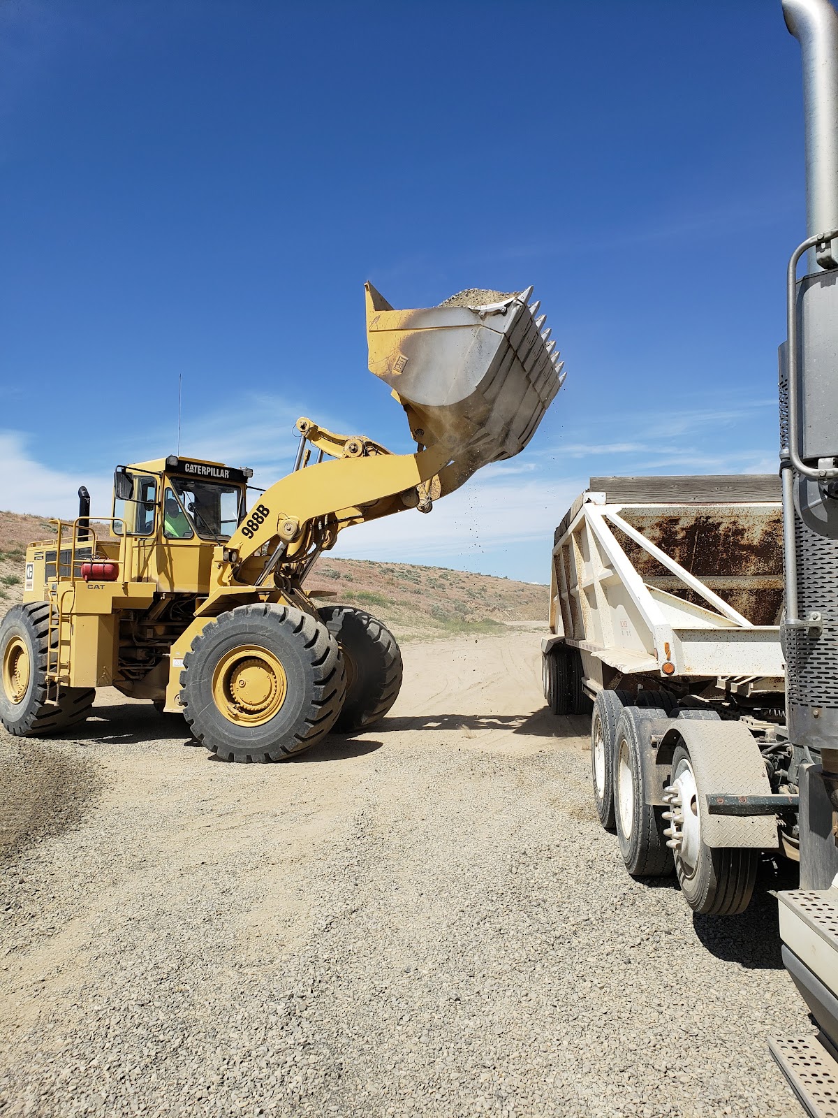 Wheel loader lifting a full bucket of aggregate beside a haul trailer