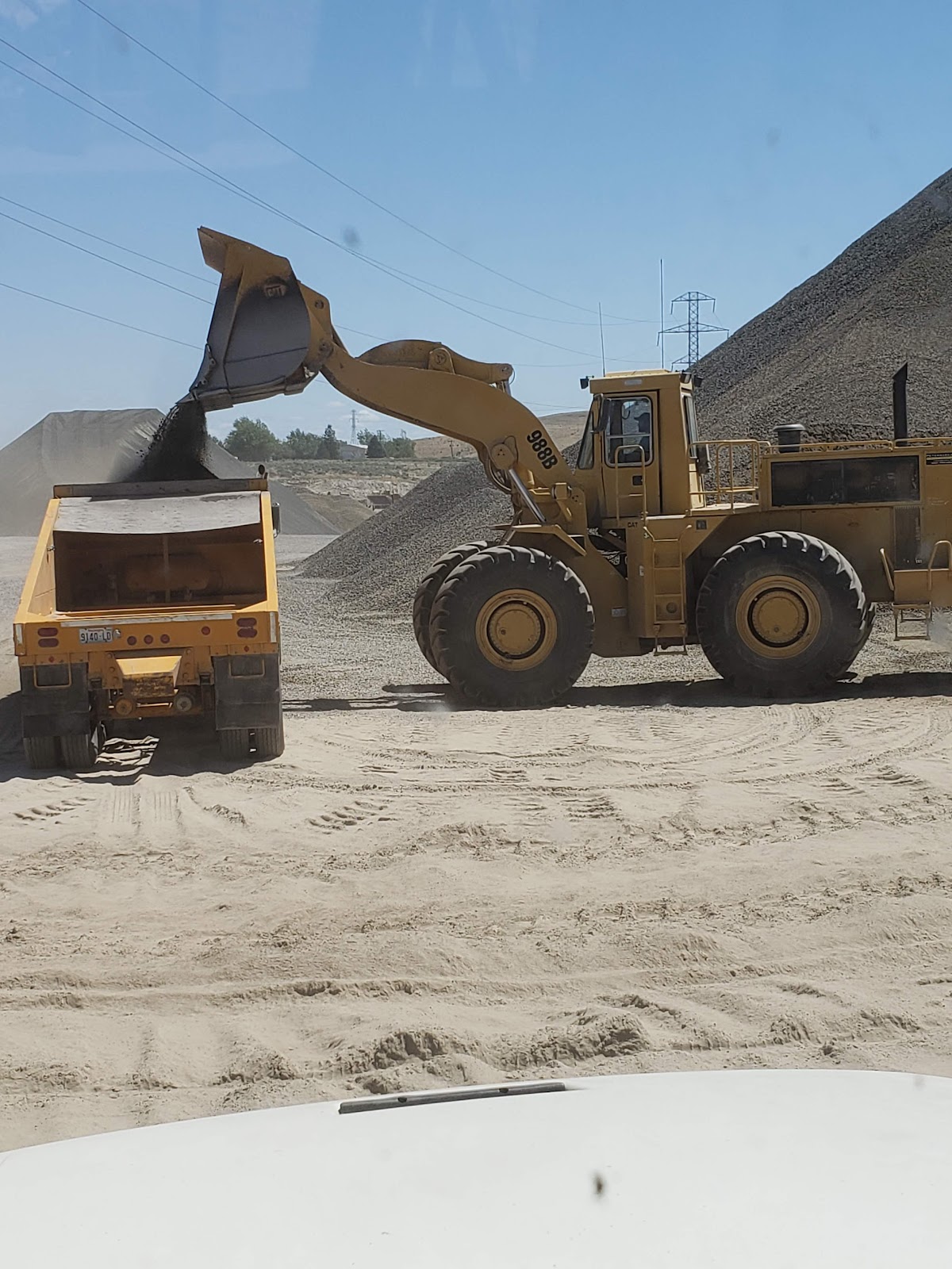 Loader pouring aggregate into a dump truck next to a gravel stockpile